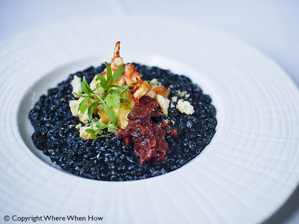 A photograph of Squid Ink Arborio, Caicos Lobster Tail with Puttanesca Sauce Risotto, Providenciales (Provo), Turks and Caicos Islands.